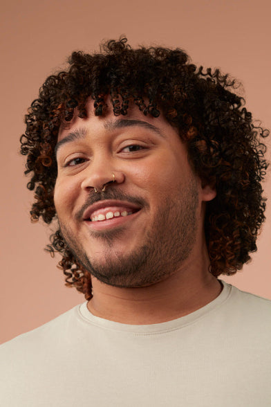 Man with curly hair and a nose ring against a beige background